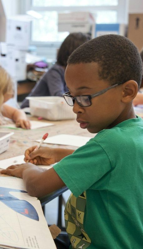 Photo by CDC boy in green sweater writing on white paper